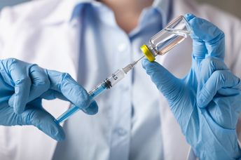 Hand holding syringe and vaccine.