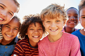 Close up of pre-teen friends in a park smiling to camera.