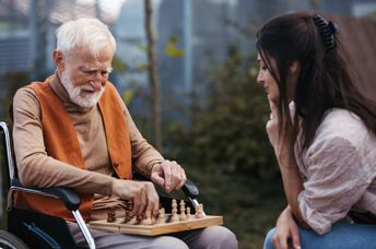 Patient young woman playing chess with a senior.