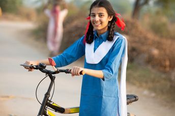 Happy schoolgirl in a rural area in India going from her village home to school, on a bicycle.