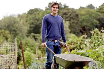 A young man pushing a wheelbarrow on an allotment.