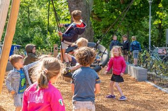 Elementary school children play outside in a playground with plenty of greenery.