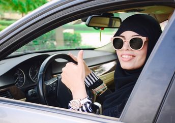 Happy business arabic lady in dark abaya and hijab driving her car and showing thumb up. Smiling arabian lady in sunglasses taking steering wheel of her new car.