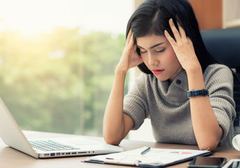 A young woman sits at her desk with a headache