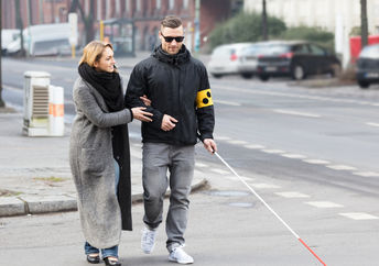 A woman helps a man cross the street