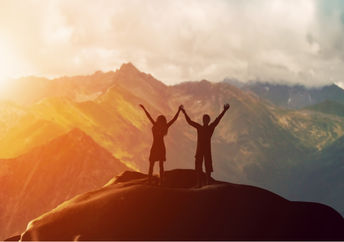 Couple standing on mountain with arms raised