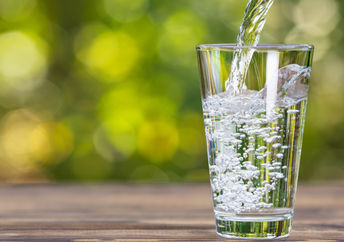 Drinking water from jug pouring into glass on wooden table outdoors