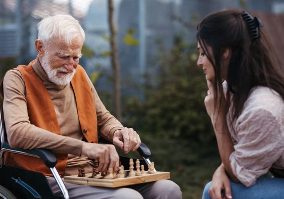 Patient young woman playing chess with a senior.