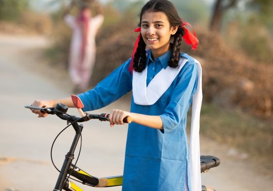 Happy schoolgirl in a rural area in India going from her village home to school, on a bicycle.