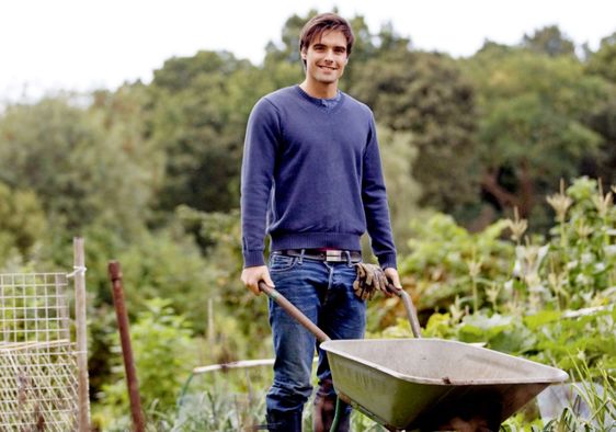 A young man pushing a wheelbarrow on an allotment.