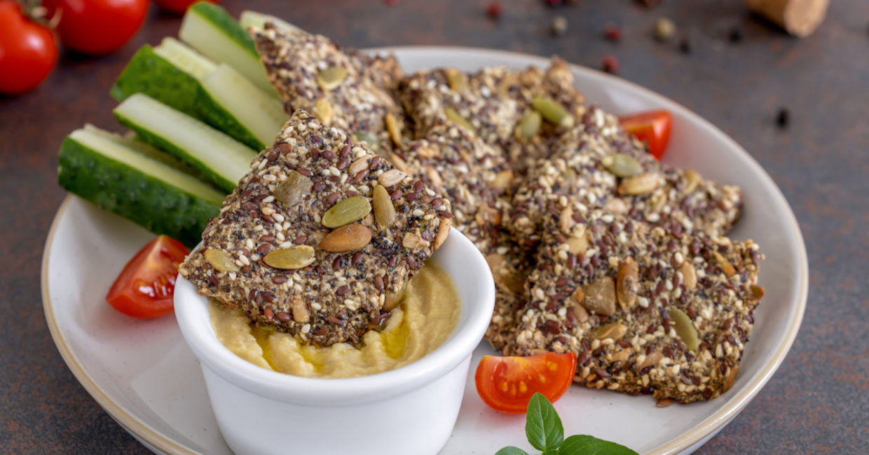 Homemade seed crackers are served with hummus and fresh vegetables.