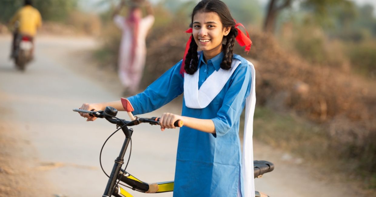 Happy schoolgirl in a rural area in India going from her village home to school, on a bicycle.