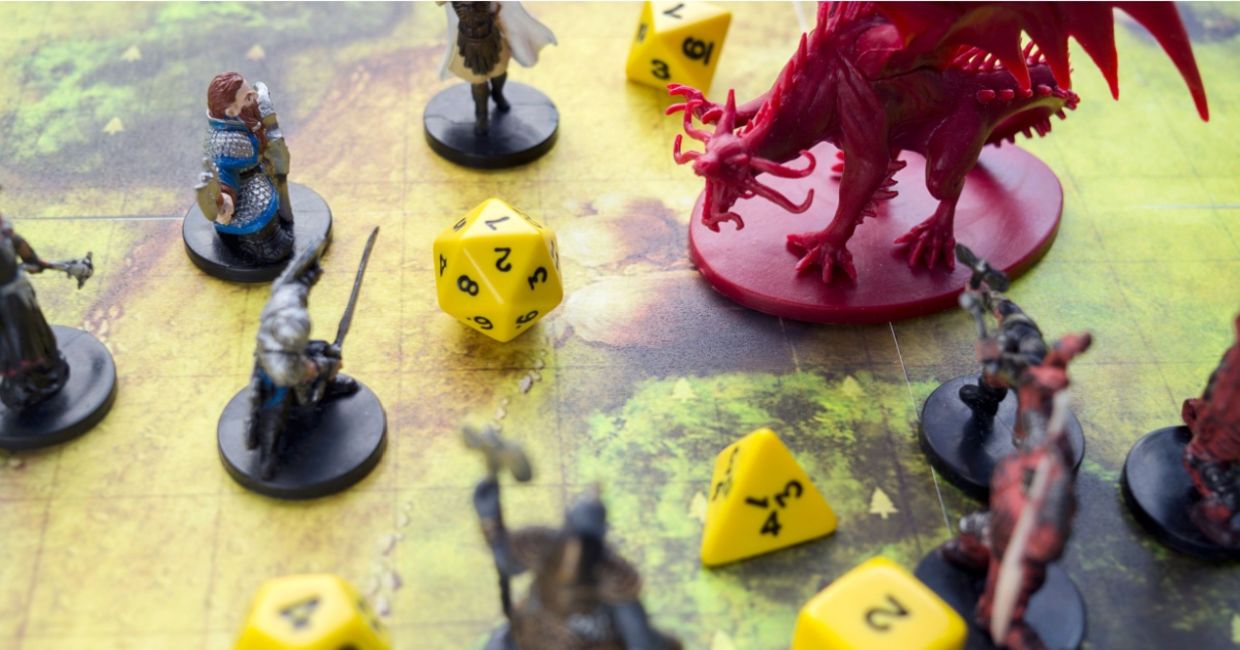 Playing Dungeons and Dragons on a board game map with a figure of a dragon, game characters and dice.