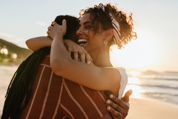 A couple embraces on a beach at sunset while the woman smiles. 