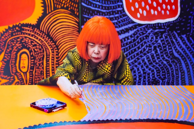 A photograph of Japanese artist Yayoi Kusama painting a work. 